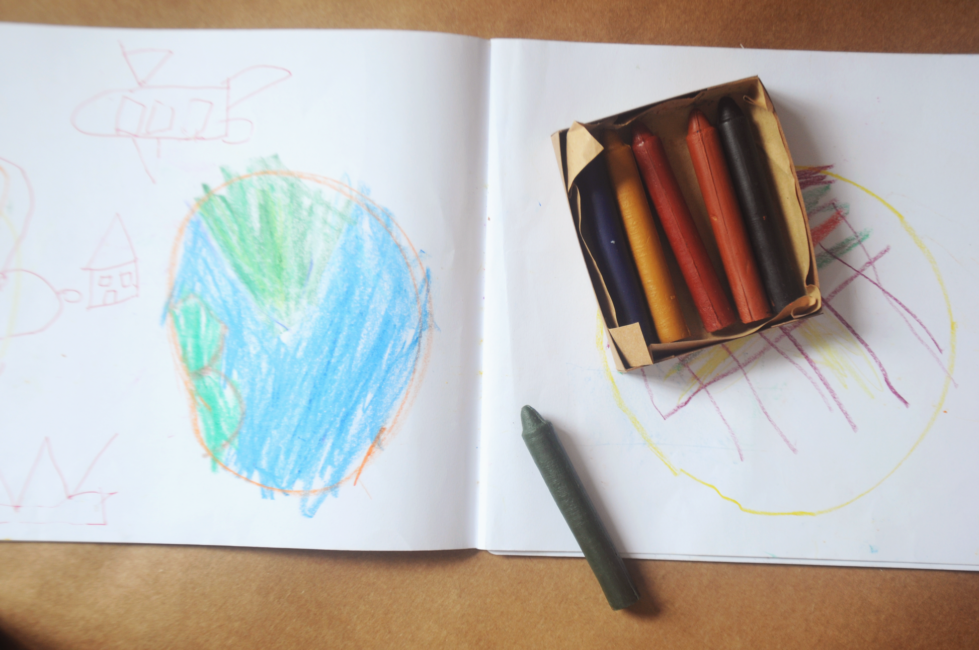 open box of standard set of six crayons with green crayon outside of the box on an open book with a coloured earth picture on the left page